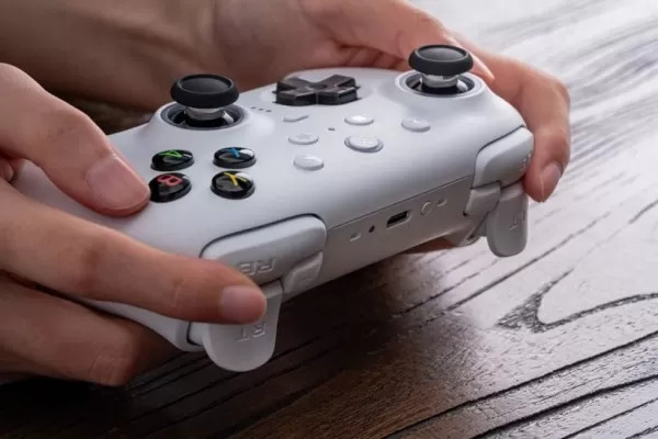 Een foto van een persoon die een witte spelcontroller vasthoudt op een houten bureau